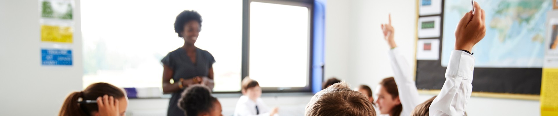 Primary School Students Wearing Uniform Raising Hands To Answer Question Set By Teacher In Classroom
