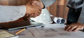 Two people shaking hands over building plans