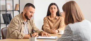 Couple signing contract whilst professional woman looks on in foreground   resized