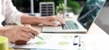 Person with laptop reading green statistics on paper