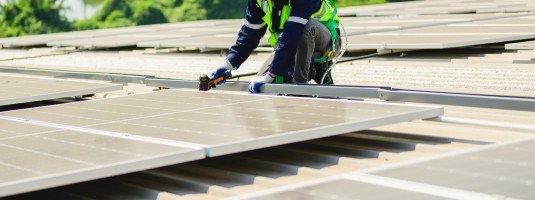 Person installing PV solar panels on a flat roof