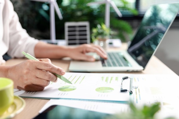 Person with laptop reading green statistics on paper