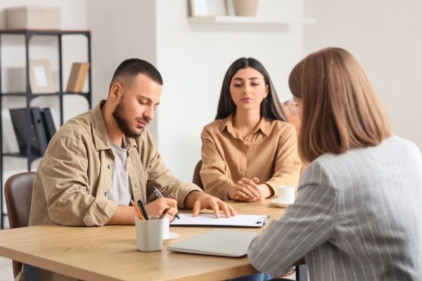 Couple signing contract whilst professional woman looks on in foreground   resized