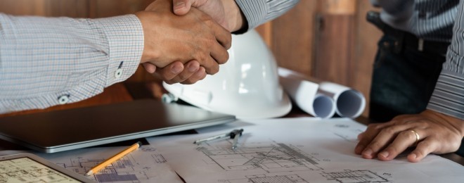 Two people shaking hands over building plans