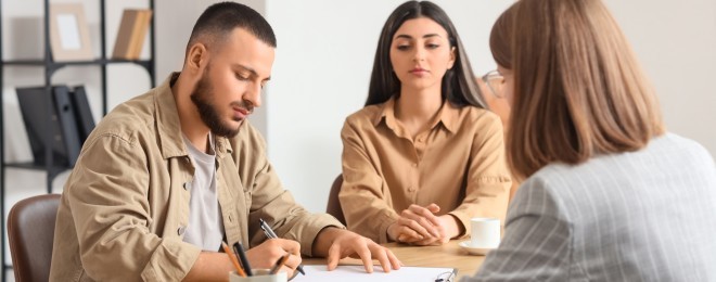 Couple signing contract whilst professional woman looks on in foreground   resized