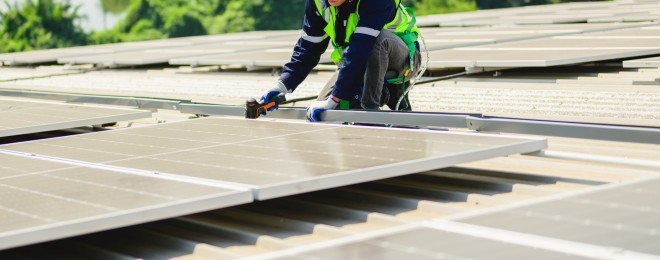 Person installing PV solar panels on a flat roof