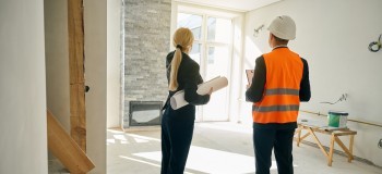 Female client and male engineer standing in room under construction