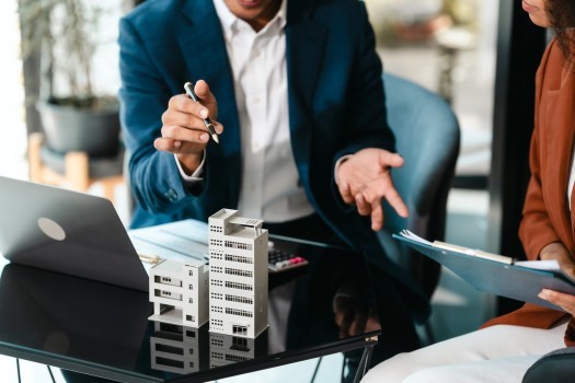 Attractive Asian businessman and African American female real estate and land investor talk discussing together on table with laptop and small building model  Reserve fund